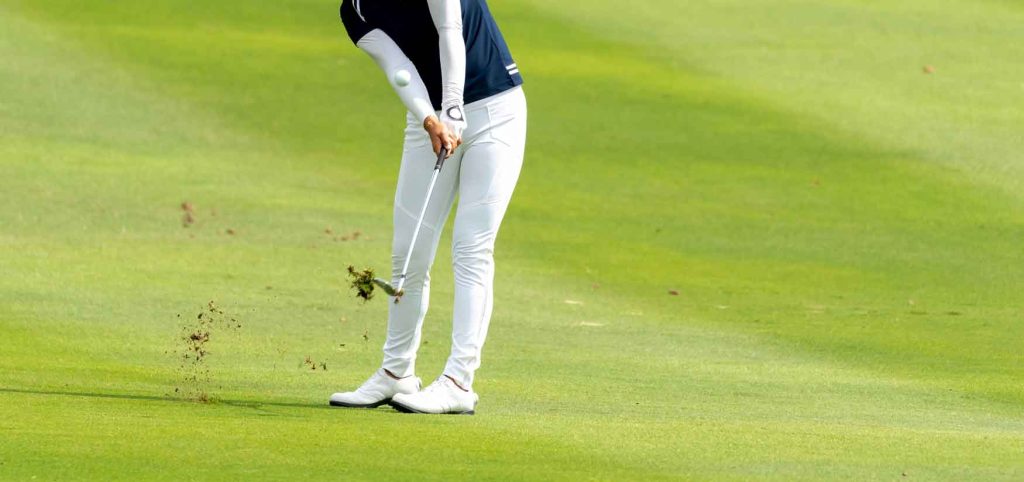 Taking a golf shot and creating a divot.