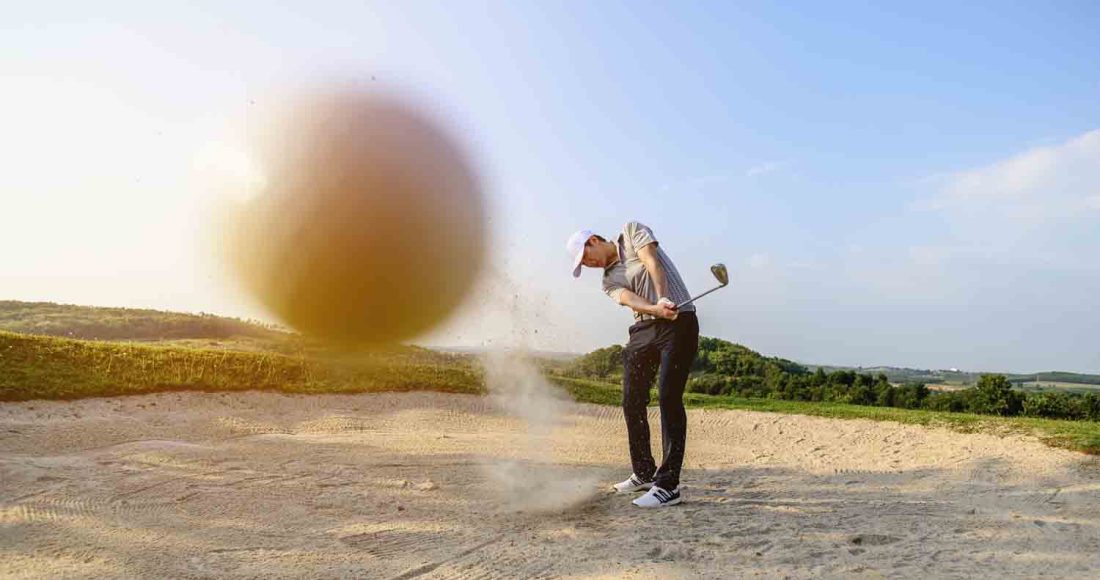 man sweeping at sand on the golf course whilst trying a bunker shot!