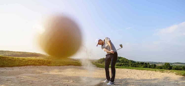 man sweeping at sand on the golf course whilst trying a bunker shot!